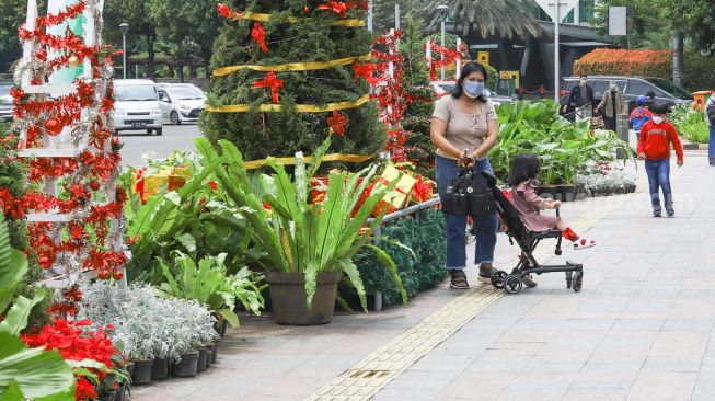 Warga melintas didepan hiasan pohon yang terpajang di Kawasan Bundaran HI, Jakarta Pusat, Sabtu (25/12/2021). [Suara.com/Alfian Winanto]