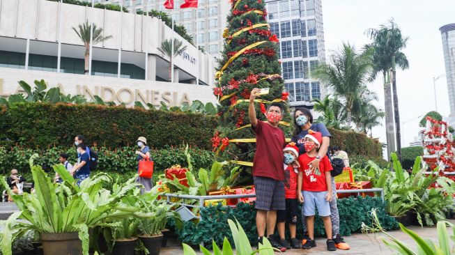 Warga berswafoto didepan hiasan pohon yang terpajang di Kawasan Bundaran HI, Jakarta Pusat, Sabtu (25/12/2021). [Suara.com/Alfian Winanto]