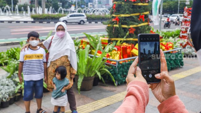 Warga berswafoto didepan hiasan pohon yang terpajang di Kawasan Bundaran HI, Jakarta Pusat, Sabtu (25/12/2021). [Suara.com/Alfian Winanto]