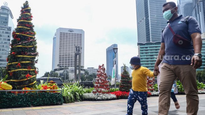 Warga melintas didepan hiasan pohon yang terpajang di Kawasan Bundaran HI, Jakarta Pusat, Sabtu (25/12/2021). [Suara.com/Alfian Winanto]