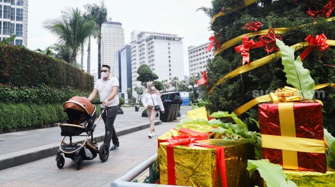 Warga melintas didepan hiasan pohon yang terpajang di Kawasan Bundaran HI, Jakarta Pusat, Sabtu (25/12/2021). [Suara.com/Alfian Winanto]