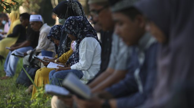 Sejumlah warga membaca surat yasin dan berdoa untuk keluarganya yang meninggal akibat bencana gempa dan tsunami di kuburan massal korban tsunami Aceh Besar, Aceh, Minggu (26/12/2021). [ANTARA FOTO/Syifa Yulinnas]