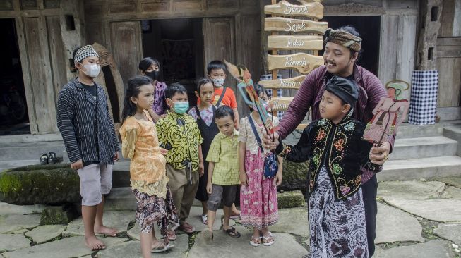 Dalang Indra Suroinggeno (kanan) mengajar anak-anak tentang wayang kulit bertema Natal di Bantul, Yogyakarta, pada (24/12/2021). [AGUNG SUPRIYANTO / AFP]