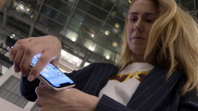 Manajer pemasaran di Epicenter Stockholm, Amanda Back memindai dengan smartphone sebuah microchip yang dikembangkan oleh perusahaan DSruptive Subdermals dan ditanamkan di tangannya untuk mengungkapkan kartu kesehatannya di Stockholm, Swedia, pada (20/12/2021). [VIKEN KANTARCI / AFP]