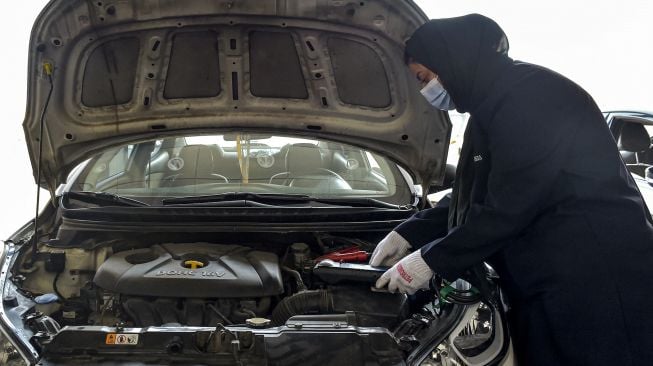 Seorang mekanik perempuan Saudi memeriksa mobil di bengkel perbaikan dan servis di kota pesisir Laut Merah, Arab Saudi, Jeddah, pada (27/12/2021). [AMER HILABI / AFP]