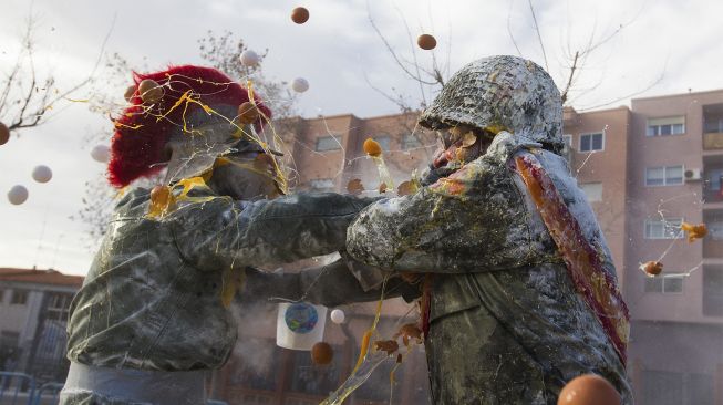 Orang-orang yang bersuka ria mengenakan pakaian militer mengambil bagian dalam pertempuran "Els Enfarinats" di Kota Ibi, Spanyol, pada (28/12/2021). [JAIME REINA / AFP]