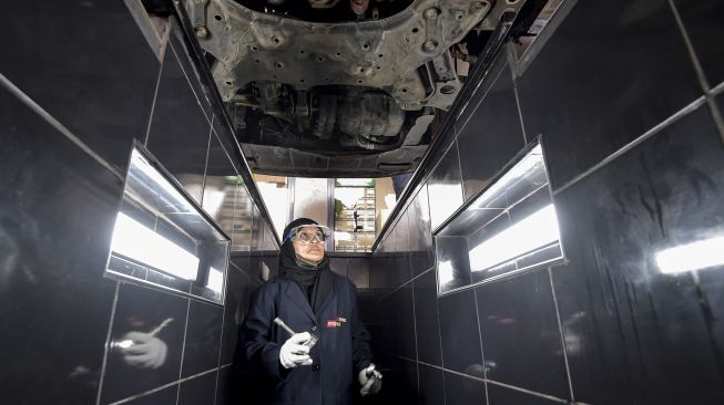 Seorang mekanik perempuan Saudi berjalan di bawah kendaraan di bengkel perbaikan dan servis di kota pesisir Laut Merah, Arab Saudi, Jeddah, pada (27/12/2021). [AMER HILABI / AFP]