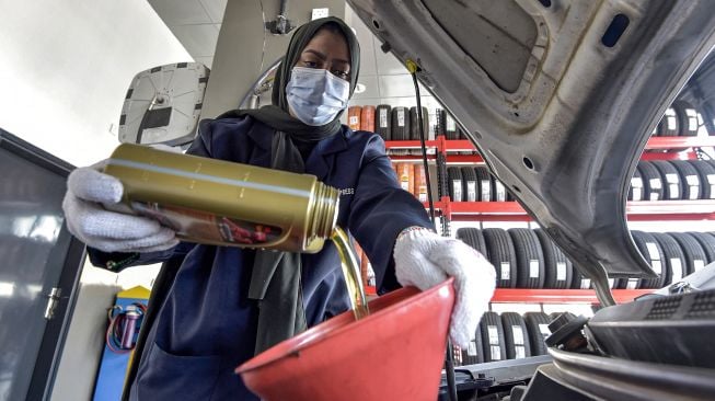 Seorang mekanik perempuan Saudi menambahkan oli baru ke mesin kendaraan di bengkel perbaikan dan servis di kota pesisir Laut Merah, Arab Saudi, Jeddah, pada (27/12/2021). [AMER HILABI / AFP]