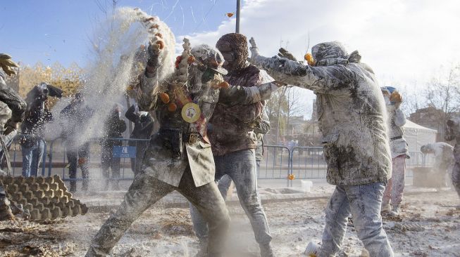 Orang-orang yang bersuka ria mengenakan pakaian militer mengambil bagian dalam pertempuran "Els Enfarinats" di Kota Ibi, Spanyol, pada (28/12/2021). [JAIME REINA / AFP]