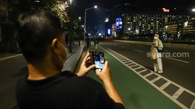 Warga berswafoto saat permberlakuan aturan Crowd Free Night di Kawasan Bundaran HI, Jakarta Pusat, Jumat (31/12/2021). 