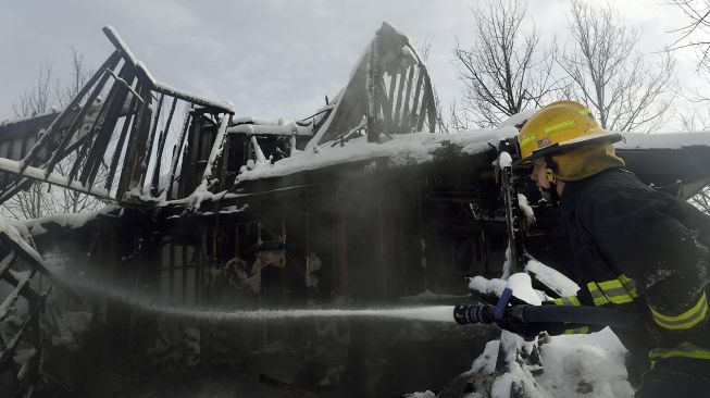 Petugas pemadam kebakaran menyemprotkan air ke rumah yang tertutup salju dan masih membara api dari Kebakaran Marshall di lingkungan Rock Creek, Kota Superior, Boulder County, Colorado, Amerika Serikat, pada (1/1/2022). [JASON CONNOLLY / AFP]