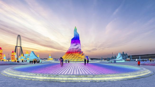 Orang-orang mengunjungi patung es di Harbin Ice and Snow World, Harbin, Provinsi Heilongjiang, China, pada (28/12/2021). [AFP]