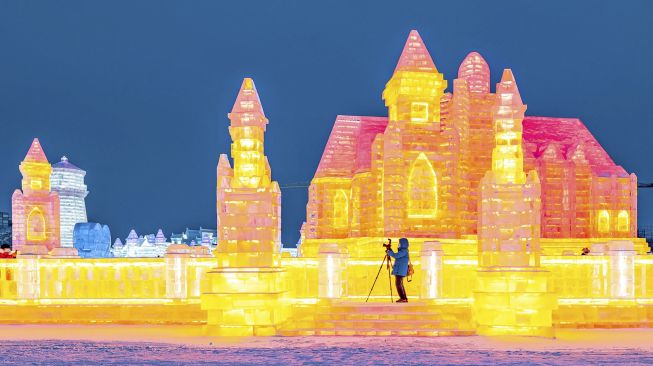 Seorang pria mengambil foto patung es di Harbin Ice and Snow World, Harbin, Provinsi Heilongjiang, China, pada (28/12/2021). [AFP]