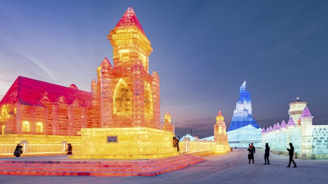 Orang-orang mengunjungi patung es di Harbin Ice and Snow World, Harbin, Provinsi Heilongjiang, China, pada (28/12/2021). [AFP]