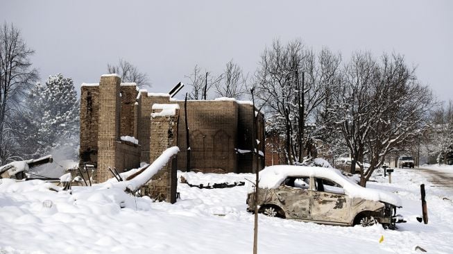 Sebuah mobil yang terbakar oleh kebakaran Marshall tertutup salju di dekat rumah-rumah yang hancur di lingkungan Rock Creek, Kota Superior, Boulder County, Colorado, Amerika Serikat, pada (1/1/2022). [JASON CONNOLLY / AFP]