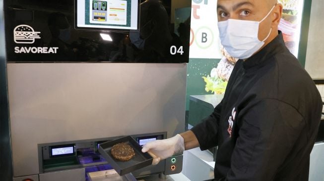 Seorang pria mengekstrak patty nabati yang dimasak dengan rasa daging dan diproduksi oleh robot sesuai dengan kebutuhan pelanggan di kota pesisir Israel, Herzliya, pada (28/12/2021). [JACK GUEZ / AFP]