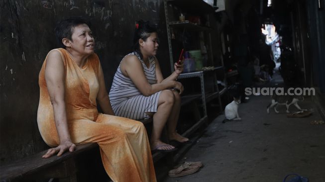 Dua warga duduk di permukiman padat penduduk Kampung Muka RW 04, Ancol, Pademangan, Jakarta, Selasa (4/1/2022). [Suara.com/Angga Budhiyanto]