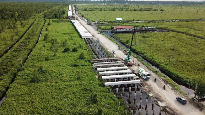 Foto udara kendaraan melintas di sebelah proyek pembangunan jembatan layang (pile slab) di Jalan Trans Kalimantan Bukit Rawi, Pulang Pisau, Kalimantan Tengah, Selasa (4/1/2022). ANTARA FOTO/Makna Zaezar