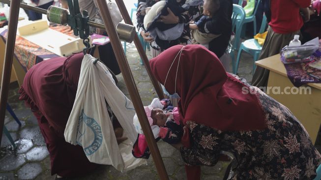 Tenaga kesehatan menimbang berat badan balita selama berlangsungnya program “BULOG Peduli Gizi” di Desa Purwosari, Kecamatan Sukorejo, Kabupaten Kendal, Jawa Tengah, Kamis (6/1/2021). [Suara.com/Angga Budhiyanto]