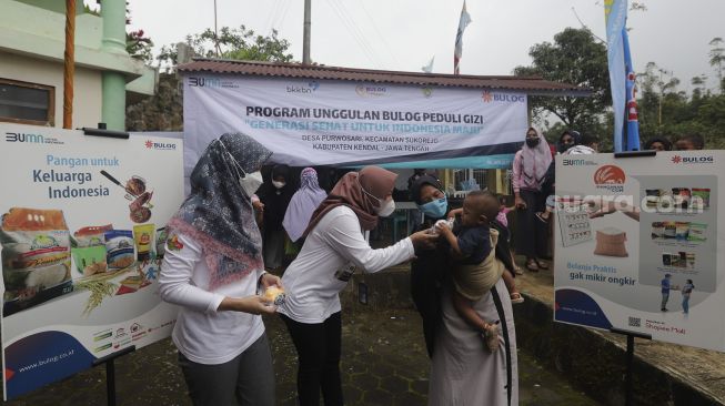 Petugas memberikan mainan kepada seorang anak selama berlangsungnya program “BULOG Peduli Gizi” di Desa Purwosari, Kecamatan Sukorejo, Kabupaten Kendal, Jawa Tengah, Kamis (6/1/2021). [Suara.com/Angga Budhiyanto]