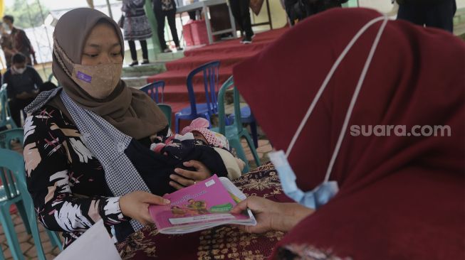 Petugas memberikan buku kesehatan ibu dan anak selama berlangsungnya program “BULOG Peduli Gizi” di Desa Purwosari, Kecamatan Sukorejo, Kabupaten Kendal, Jawa Tengah, Kamis (6/1/2021). [Suara.com/Angga Budhiyanto]