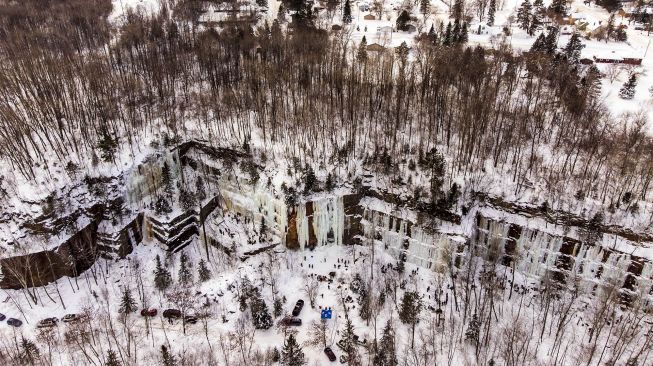 Foto udara pendaki memanjat dinding batu yang ditutupi pilar es selama Festival Panjat Tebing Es Sandstone, Minnesota, Amerika Serikat, pada (8/1/2022). [KEREM YUCEL / AFP]