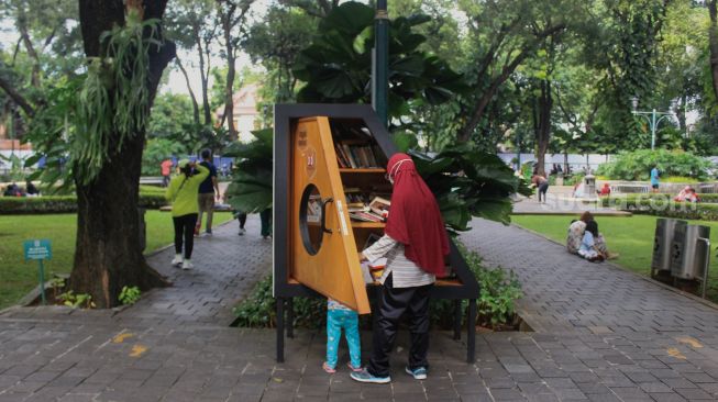 Pengunjung memilih buku di perpustakaan mini di Taman Suropati, Jakarta, Minggu (9/1/2022). [Suara.com/Septian]