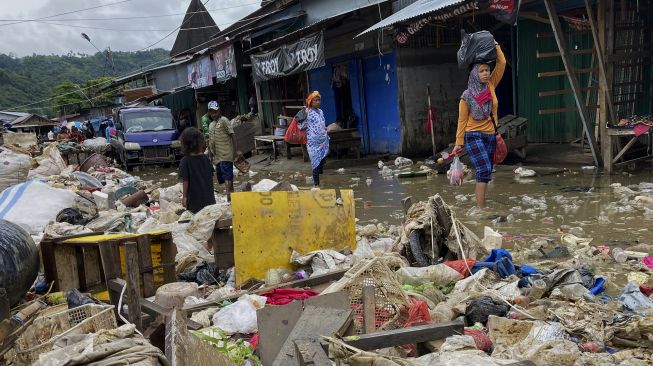 Sejumlah warga melintasi tumpukan sampah akibat banjir di Pasar Youtefa, Abepura, Jayapura, Papua, Minggu (9/1/2022). [ANTARA FOTO/Adharnazamudin]