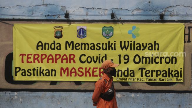 Petugas Penanganan Prasarana dan Sarana Umum (PPSU) berdiri di depan spanduk tanda zona terpapar COVID-19 di Kelurahan Krukut, Kecamatan Taman Sari, Jakarta, Senin (10/1/2021). [Suara.com/Angga Budhiyanto]