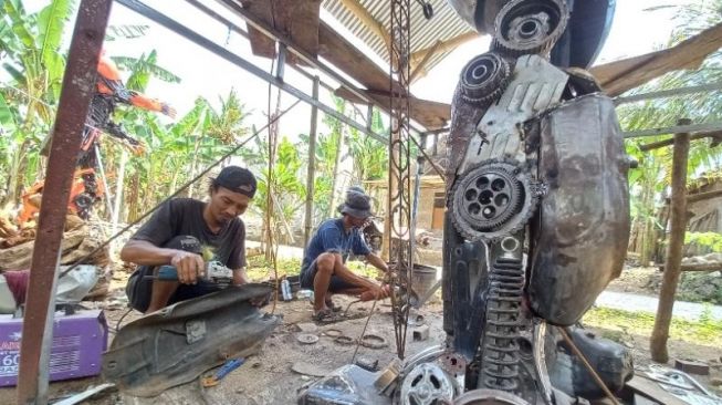 Fery (kiri) sedang memotong besi dari kerangka sepeda motor untuk dibuat robot. (SuaraJogja.id/Rahmat Jiwandono)