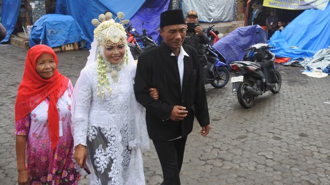 Pasangan penyintas awan panas guguran erupsi Gunung Semeru Hasanatun Munawaroh (kedua kiri) dan Nurhadi (ketiga kiri) usai melaksanakan prosesi akad nikah di Posko pengungsian Penanggal, Candipuro, Lumajang, Jawa Timur, Selasa (11/1/2022).  ANTARA FOTO/Seno