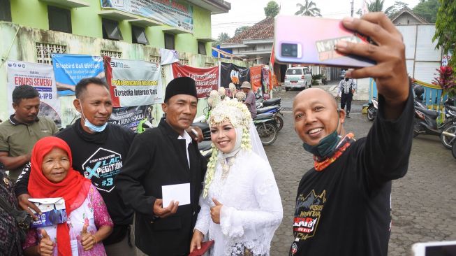 Relawan (kanan) berswafoto dengan pasangan penyintas awan panas guguran erupsi Gunung Semeru Hasanatun Munawaroh (kedua kanan) dan Nurhadi (ketiga kanan) usai melaksanakan prosesi akad nikah di Posko pengungsian Penanggal, Candipuro, Lumajang, Jawa Timur, Selasa (11/1/2022). ANTARA FOTO/Seno