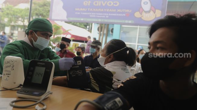 Tenaga kesehatan memeriksa kesehatan warga yang akan mendapatkan vaksin COVID-19 dosis ketiga di Puskesmas Kecamatan Kramat Jati, Jakarta, Rabu (12/1/2022). [Suara.com/Angga Budhiyanto]