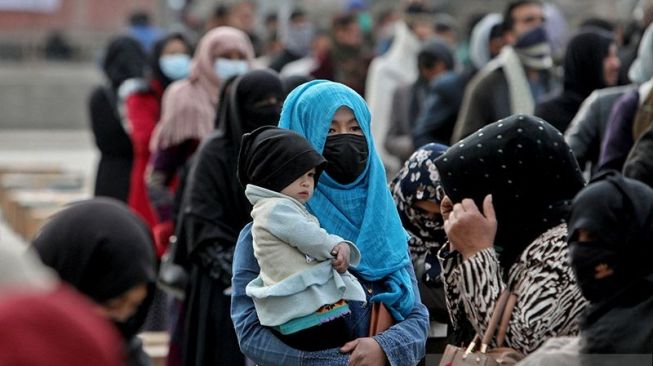 Seorang perempuan Afghanistan menggendong anaknya di tengah orang-orang yang menunggu paket bantuan yang disalurkan oleh sebuah kelompok bantuan kemanusiaan Turki. [Dok.Antara/Reuters]