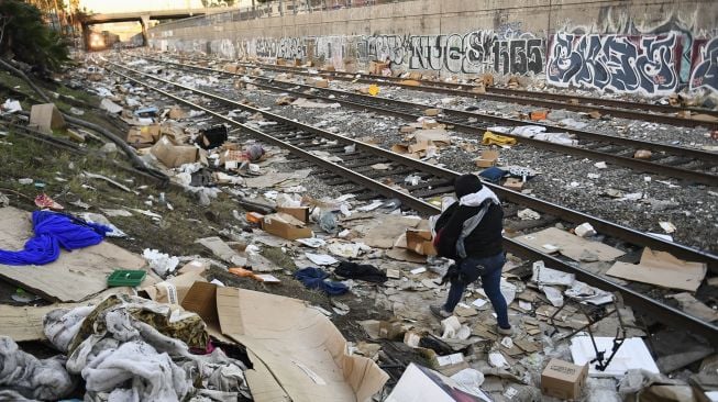 Seseorang membawa barang-barang yang dikumpulkan dari rel kereta api saat lokomotif Union Pacific melewati rel yang dipenuhi ribuan kotak terbuka dan paket yang dicuri dari kontainer pengiriman kargo di pusat Kota Los Angeles, California, Amerika Serikat, pada (14/1/2022). [PATRICK T. FALLON / AFP]