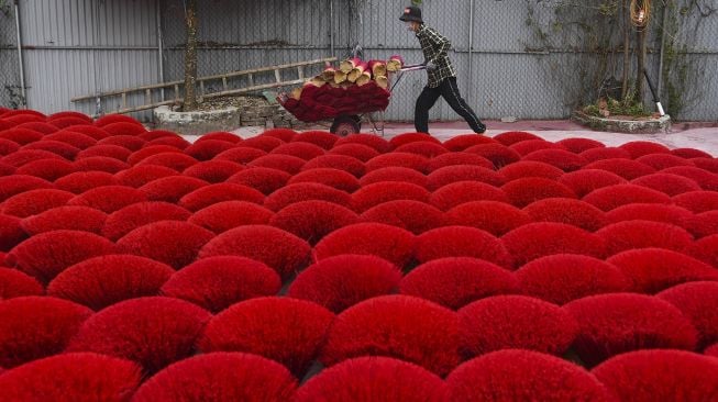 Seorang pekerja mendorong gerobak melewati dupa kering di sebuah halaman di Desa Quang Phu Cau, Hanoi, Vietnam, pada (12/1/2022). [NHAC NGUYEN / AFP]