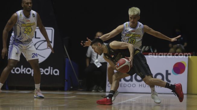 Pebasket West Bandits Combiphar Solo Widyanta Putra Teja berusaha melewati hadangan dari pebasket Prawira Bandung Hans Abraham pada pertandingan Seri 1 Jakarta Indonesian Basketball League (IBL) 2022 di Hall Basket Senayan, GBK, Jakarta, Senin (17/1/2022). [Suara.com/Angga Budhiyanto]