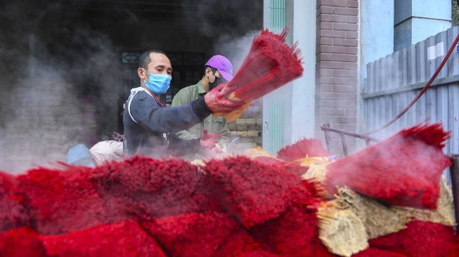 Seorang pekerja mewarnai dupa di sebuah bengkel di Desa Quang Phu Cau, Hanoi, Vietnam, pada (12/1/2022). [NHAC NGUYEN / AFP]