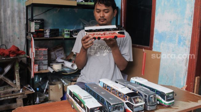 Andy Kunaryo (34) mengamati miniatur bus buatannya di Workshop Belang Bentong, Limo, Depok, Jawa Barat, Senin (17/1/2022). [Suara.com/Septian]