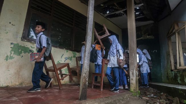 Siswa memindahkan peralatan belajar mengajar ke tenda darurat di MTs Mathlahul Anwar Sumur, Pandeglang, Banten, Senin (17/1/2022). [ANTARA FOTO/Muhammad Bagus Khoirunas]