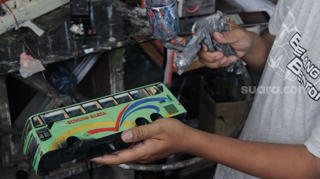 Andy Kunaryo (34) menyelesaikan pembuatan miniatur bus di Workshop Belang Bentong, Limo, Depok, Jawa Barat, Senin (17/1/2022). [Suara.com/Septian]