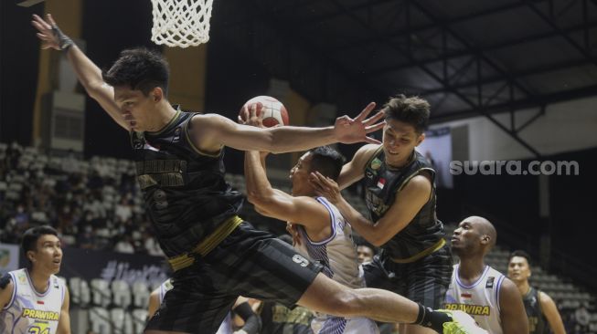 Pebasket West Bandits Combiphar Solo Rio Disi (kiri) dan Mei Joni (ketiga kanan) memblok usaha lay up dari peasket Prawira Bandung Diftha Pratama (tengah) pada pertandingan Seri 1 Jakarta Indonesian Basketball League (IBL) 2022 di Hall Basket Senayan, GBK, Jakarta, Senin (17/1/2022). [Suara.com/Angga Budhiyanto]