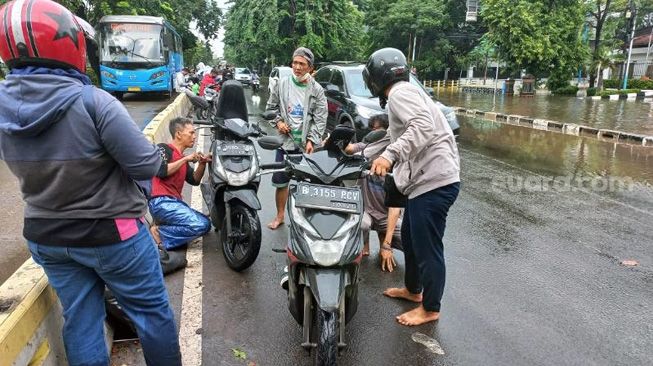 Imam alias Bang Nyamuk tampak tengah memperbaiki sepeda motor warga yang mogok akibat nekat menerjang genangan air di Jalan Letjen Suprapto, Cempaka Putih, Jakarta Pusat, Selasa (18/1/2022). [Suara.com/Yaumal Asri Adi Hutasuhut]