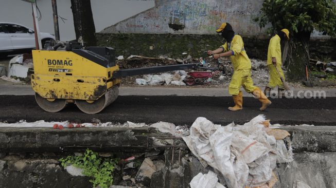 Petugas Suku Dinas Bina Marga Jakarta Pusat memperbaiki jalan ambles di Jalan Inspeksi Kali Ciliwung, Kenari, Kecamatan Senen, Jakarta, Rabu (19/1/2022). [Suara.com/Angga Budhiyanto]