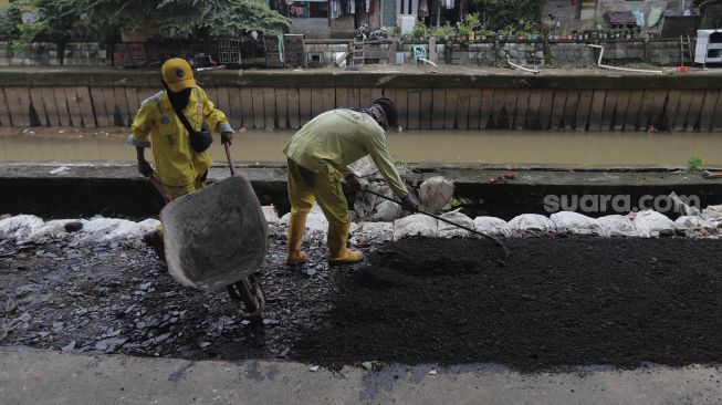 Petugas Suku Dinas Bina Marga Jakarta Pusat memperbaiki jalan ambles di Jalan Inspeksi Kali Ciliwung, Kenari, Kecamatan Senen, Jakarta, Rabu (19/1/2022). [Suara.com/Angga Budhiyanto]