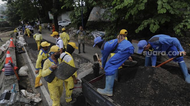 Petugas Suku Dinas Bina Marga Jakarta Pusat memperbaiki jalan ambles di Jalan Inspeksi Kali Ciliwung, Kenari, Kecamatan Senen, Jakarta, Rabu (19/1/2022). [Suara.com/Angga Budhiyanto]