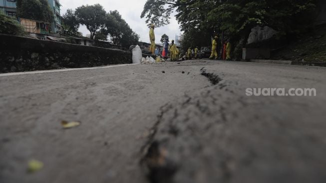 Petugas Suku Dinas Bina Marga Jakarta Pusat memperbaiki jalan ambles di Jalan Inspeksi Kali Ciliwung, Kenari, Kecamatan Senen, Jakarta, Rabu (19/1/2022). [Suara.com/Angga Budhiyanto]