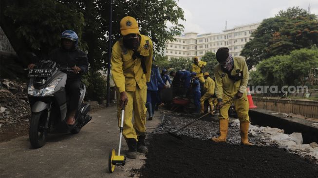 Petugas Suku Dinas Bina Marga Jakarta Pusat memperbaiki jalan ambles di Jalan Inspeksi Kali Ciliwung, Kenari, Kecamatan Senen, Jakarta, Rabu (19/1/2022). [Suara.com/Angga Budhiyanto]