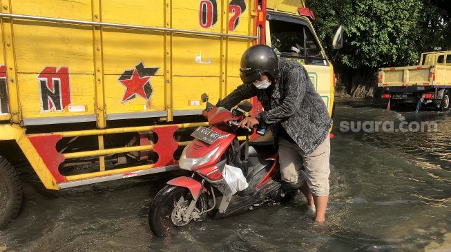 Dimas (26) salah seorang pengendara motor yang kendaraannya mogok akibat nekat menerobos banjir di Jalan Kamal Raya, Tegal Alur, Jakarta Barat, Rabu (19/1/2022). [Suara.com/Faqih Fathurrahman]