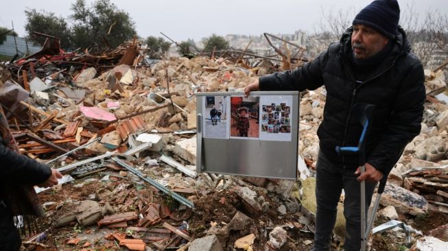 Seorang warga Palestina menunjukkan foto keluarga yang dipungut dari puing-puing rumah warga Palestina yang digusur di Sheikh Jarrah, Yerusalem Timur, Rabu (19/1/2022). Israel pada Rabu pagi menggusur rumah-rumah warga Palestina di Sheikh Jarrah. [AFP/Ahmad Gharabli]